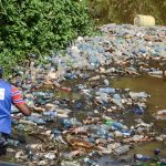 Dumpsite in Nairobi - A volunteer cleaner wades through a batch of plastic trash floating in River Njoro Nakuru Kenya www.businesstoday.co.ke