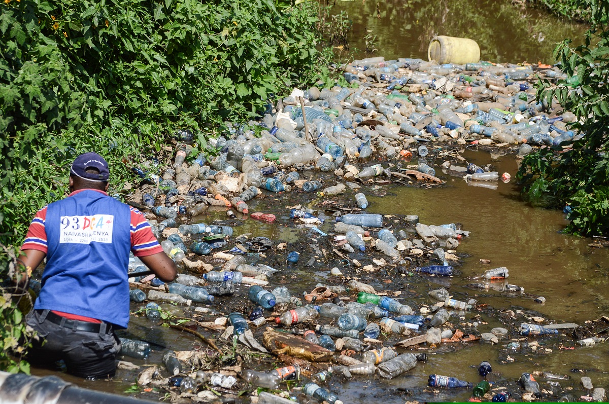 Dumpsite in Nairobi - A volunteer cleaner wades through a batch of plastic trash floating in River Njoro Nakuru Kenya www.businesstoday.co.ke