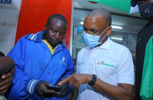 Safaricom PLC CEO Peter Ndegwa is taken through a Lipa Na M-PESA process by Alexander Ondenyi a fruit vendor in Kakamega town during his visit in the town