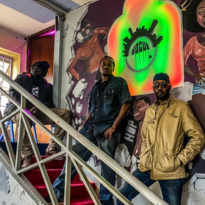 Andrew Kibe (far right) poses with Brian Wambugu (centre) at Rogue Radio studios in front of Wambugu's logo design selected in an online challenge