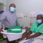 Safaricom Foundation Chairman, Joe Ogutu (standing) hands over Mama Pack to Judy Waithera, during Safaricom Foundation’s handover of a Maternal HDU and Newborn unit in KNH Othaya, Nyeri County.