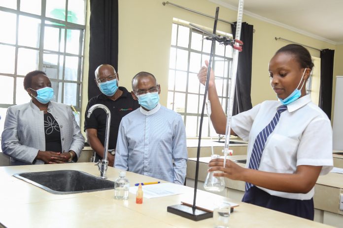 Safaricom PLC CEO, Peter Ndegwa (second right), with Safaricom Foundation Chairman, Joe Ogutu, following through, as Wanjiku Mwaura, a form three student at Shadrack Kimalel secondary school, undertakes a titration experiment during a chemistry practical lesson. Also, present is the school Principal, Mrs. Beatrice Sharao. This was moments after Safaricom Foundation donated a science Laboratory, funded at a cost of Kshs. 5.5 million.