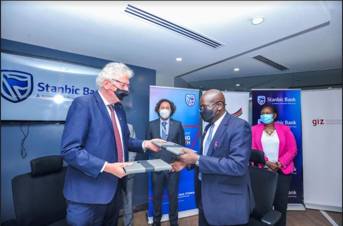 Stanbic Bank Kenya Chief Executive (CE), Charles Mudiwa (right), and GIZ Country Director, Bodo Immink (left) pose for a photo with the signed cooperation agreement documents. The two institutions have signed an agreement aimed at accelerating business recovery and growth of small enterprises post the Covid-19 Pandemic at Stanbic Bank offices in Nairobi. Looking on is Luis Bosch (second left), Thomas Jaeschke (third left), Head of Stanbic Kenya Foundation, Pauline Mbayah (third right) and Chief Administrative Secretary (CAS) Industrialization, Lawrence Karanja (second right).