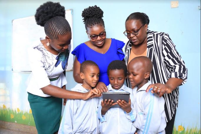 L-R Mercynet Lwane, Linet Kaloki and Regional Director Worldreader East Africa Joan Mwachi pose for a photo with children from Kidogo Center in Kangemi during Young Readers Day celebrations