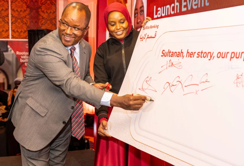 Absa Bank Kenya PLC Chief Finance Officer Yusuf Omari, signs the commitment board during the launch of the La Riba Sultanah, Kenya’s first Shariah-compliant bank account designed to cater to women entrepreneurs. Looking on is Absa Bank La Riba Banker Lutfa Anas Ali.