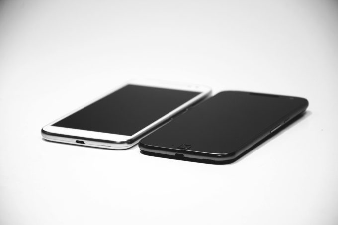 Two smartphones, one black and one white, placed on a white surface